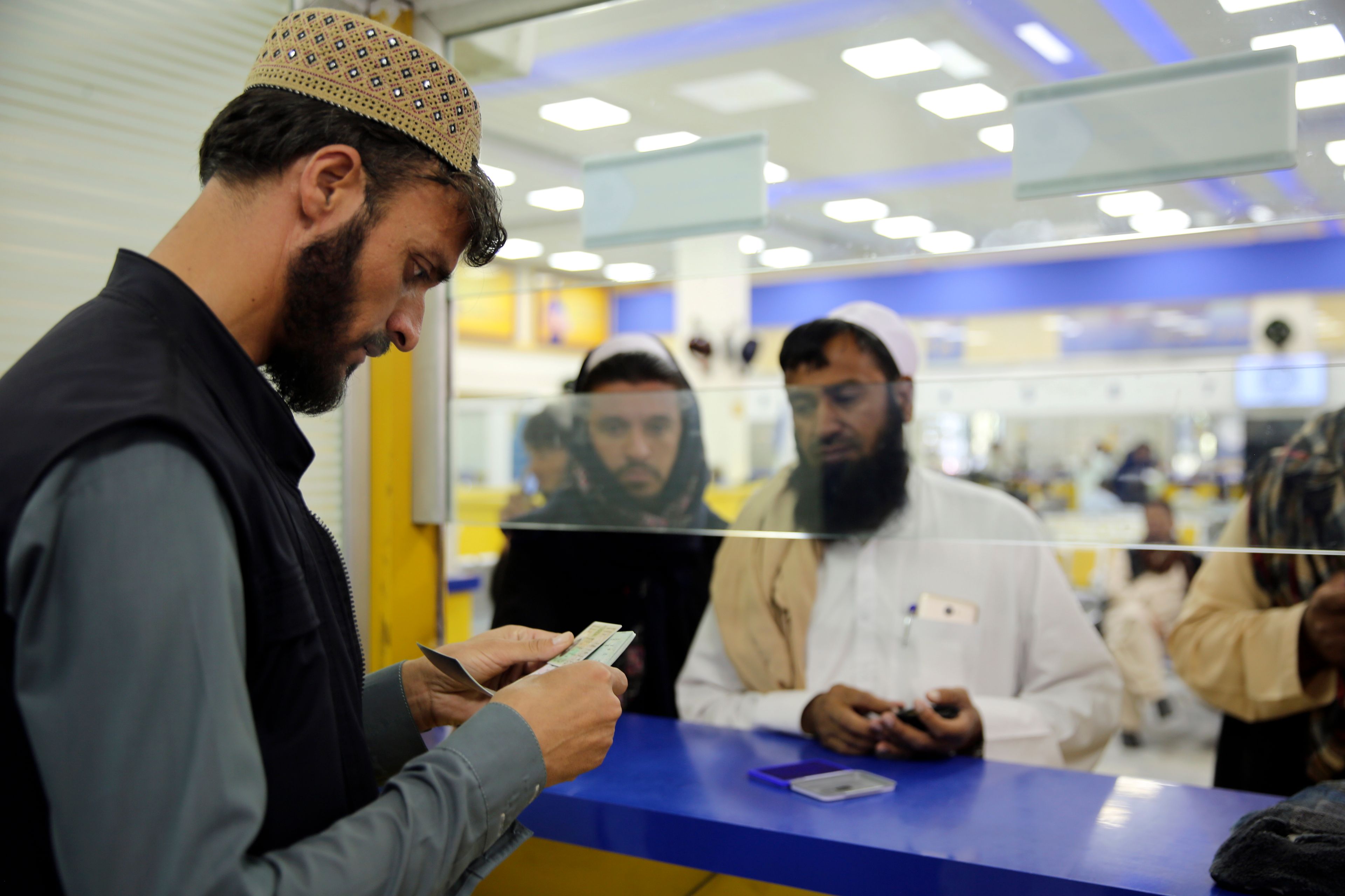 A worker checks the documents of a man to receive his passport in the main post office in the city of Kabul, Afghanistan, Wednesday, July 3, 2024. In parts of Afghanistan where there are no street names or house numbers, utility companies and their customers have adopted a creative approach for connecting. They use mosques as drop points for bills and cash, a "pay and pray" system. (AP Photo/Siddiqullah Alizai)