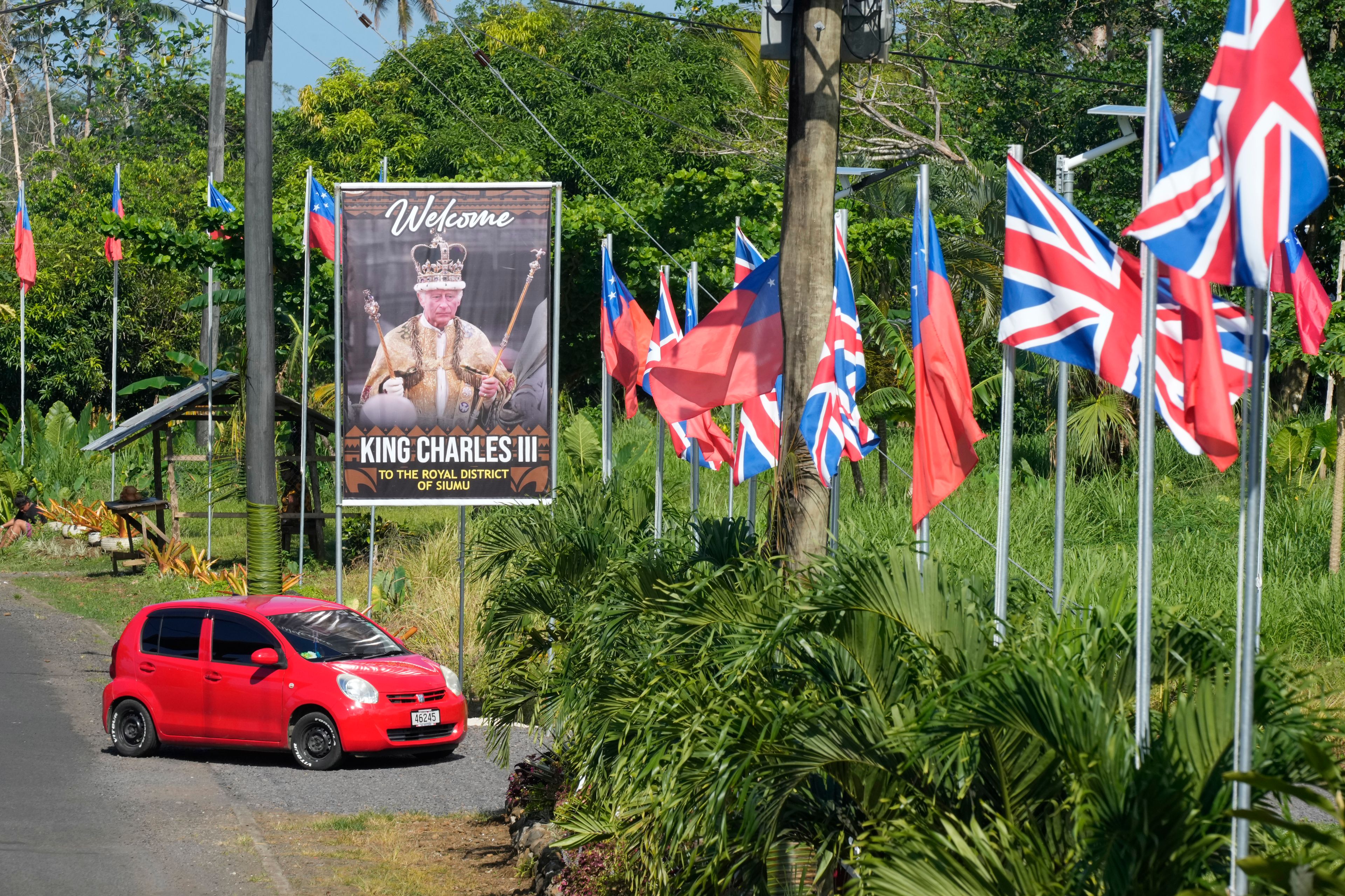 A car turns off a road decorated with flags and a portrait in the village of Siumu, Samoa, on Monday, Oct. 21, 2024, as the village prepares for the arrival of King Charles III. (AP Photo/Rick Rycroft)