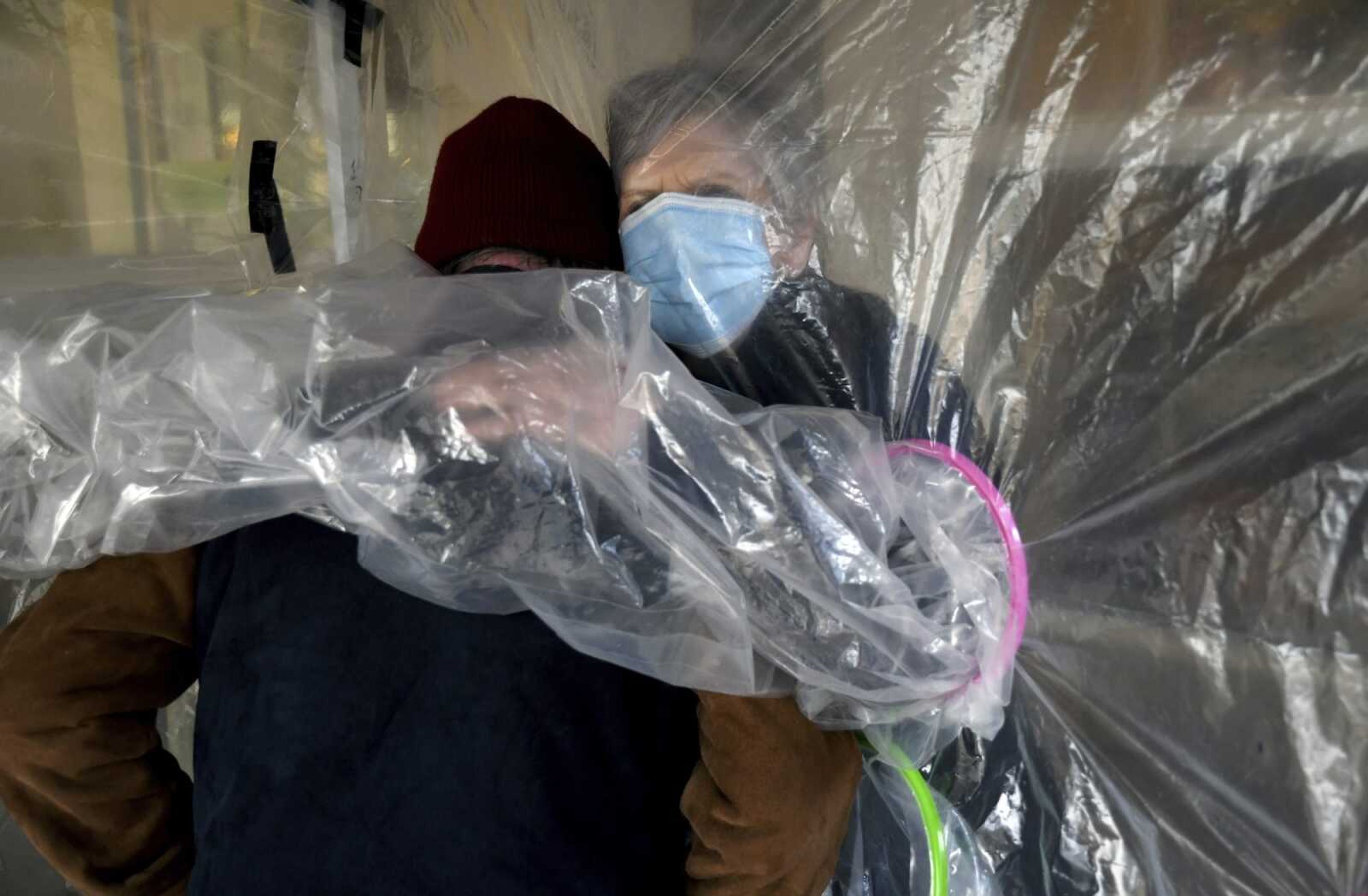 Lynda Hartman, 75, embraces her 77-year-old husband, Len Hartman, who suffers from dementia, in a "hug tent" set up outside the Juniper Village assisted living center Wednesday in Louisville, Colorado. The tent includes a construction-grade plastic barrier with built-in plastic sleeves to prevent the spread of the coronavirus. He has been living at the center for about a year, and the couple had not had any physical contact for at least eight months.