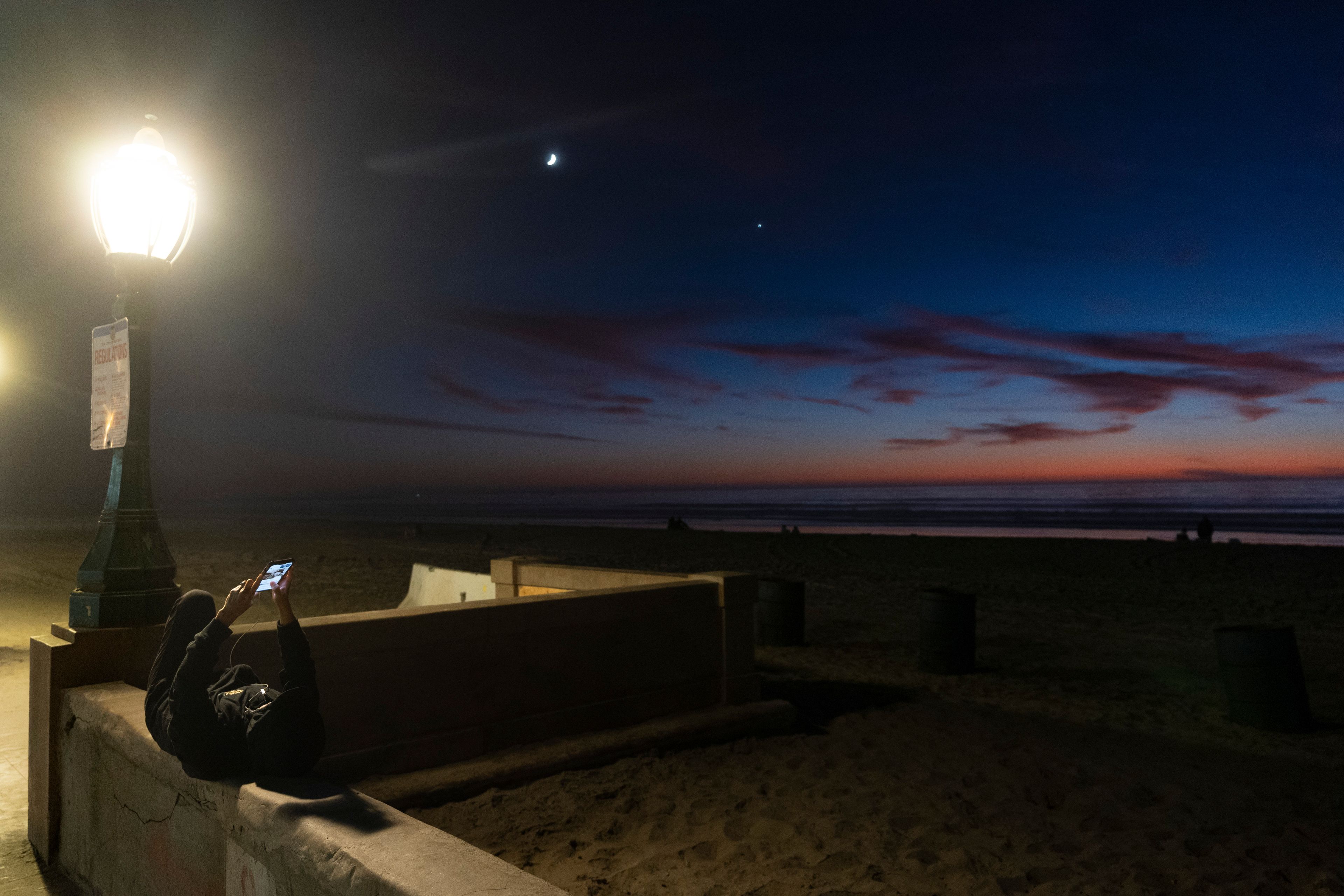 Pim Moynihan, of San Diego, watches election results on her phone as she lays on a wall along Mission Beach on Election Day, Tuesday, Nov. 5, 2024, in San Diego. (AP Photo/Gregory Bull)