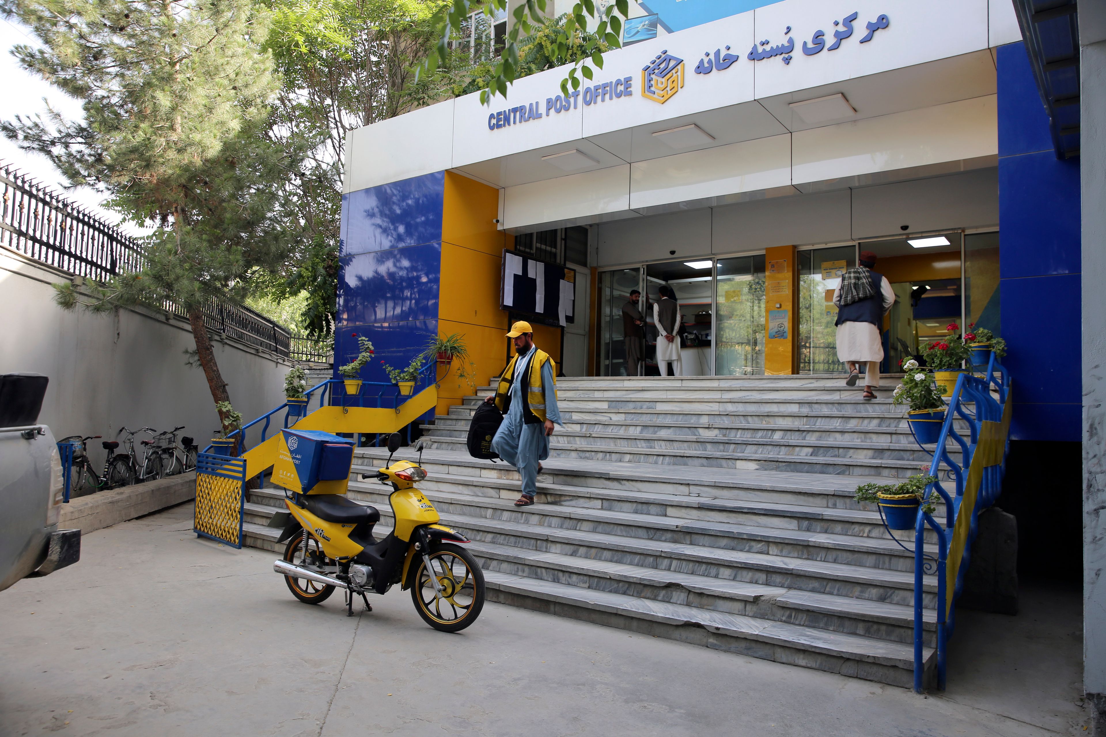 A postman walks in front of The Afghan Post office in the city of Kabul, Afghanistan, Wednesday, July 3, 2024. In parts of Afghanistan where there are no street names or house numbers, utility companies and their customers have adopted a creative approach for connecting. They use mosques as drop points for bills and cash, a "pay and pray" system. (AP Photo/Siddiqullah Alizai)