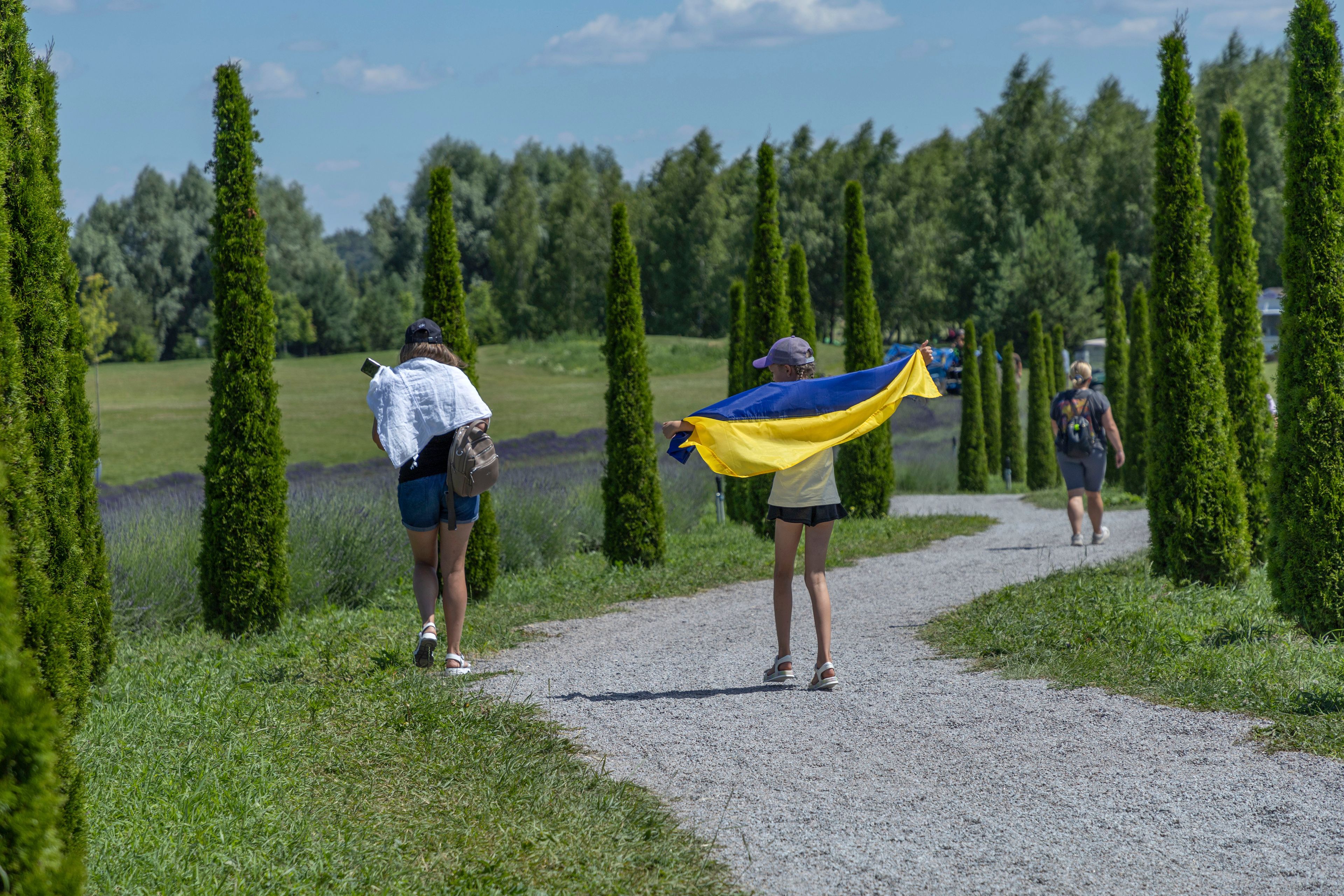 A girl uses a Ukrainian flag to shelter from the sun in Dobro Park, Motyzhyn, Kyiv region, Ukraine, Wednesday, June 26, 2024. Despite hardships brought by war flowers fill Kyiv and other Ukrainian cities. Dobro Park, a 370-acre (150 hectare) privately-run garden and recreation area west of Kyiv, was rebuilt after the Russian attack and occupation that lasted for more than a month.(AP Photo/Anton Shtuka)