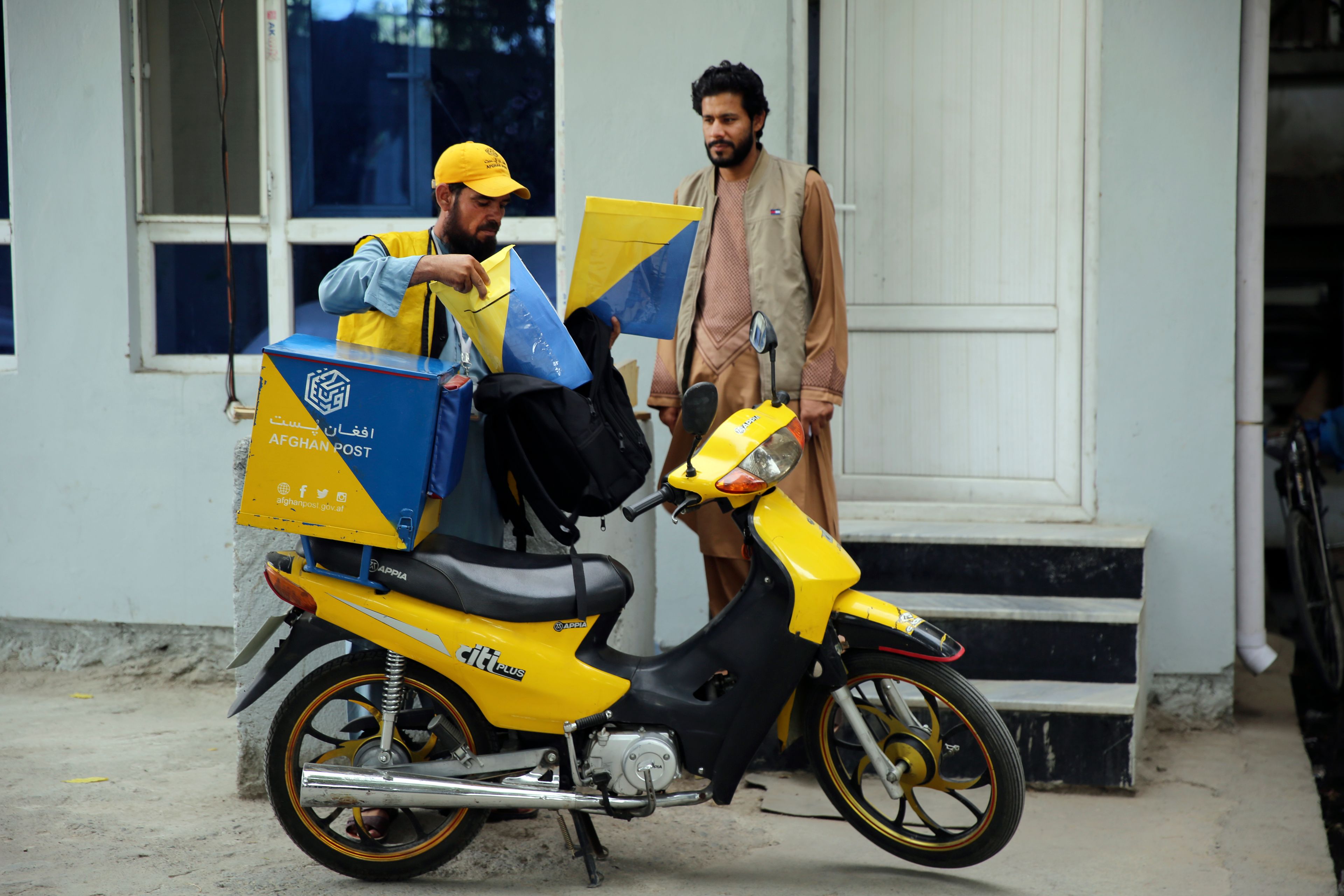 A postman delivers to a man in front of his house in the city of Kabul, Afghanistan, Wednesday, July 3, 2024. In parts of Afghanistan where there are no street names or house numbers, utility companies and their customers have adopted a creative approach for connecting. They use mosques as drop points for bills and cash, a "pay and pray" system. (AP Photo/Siddiqullah Alizai)