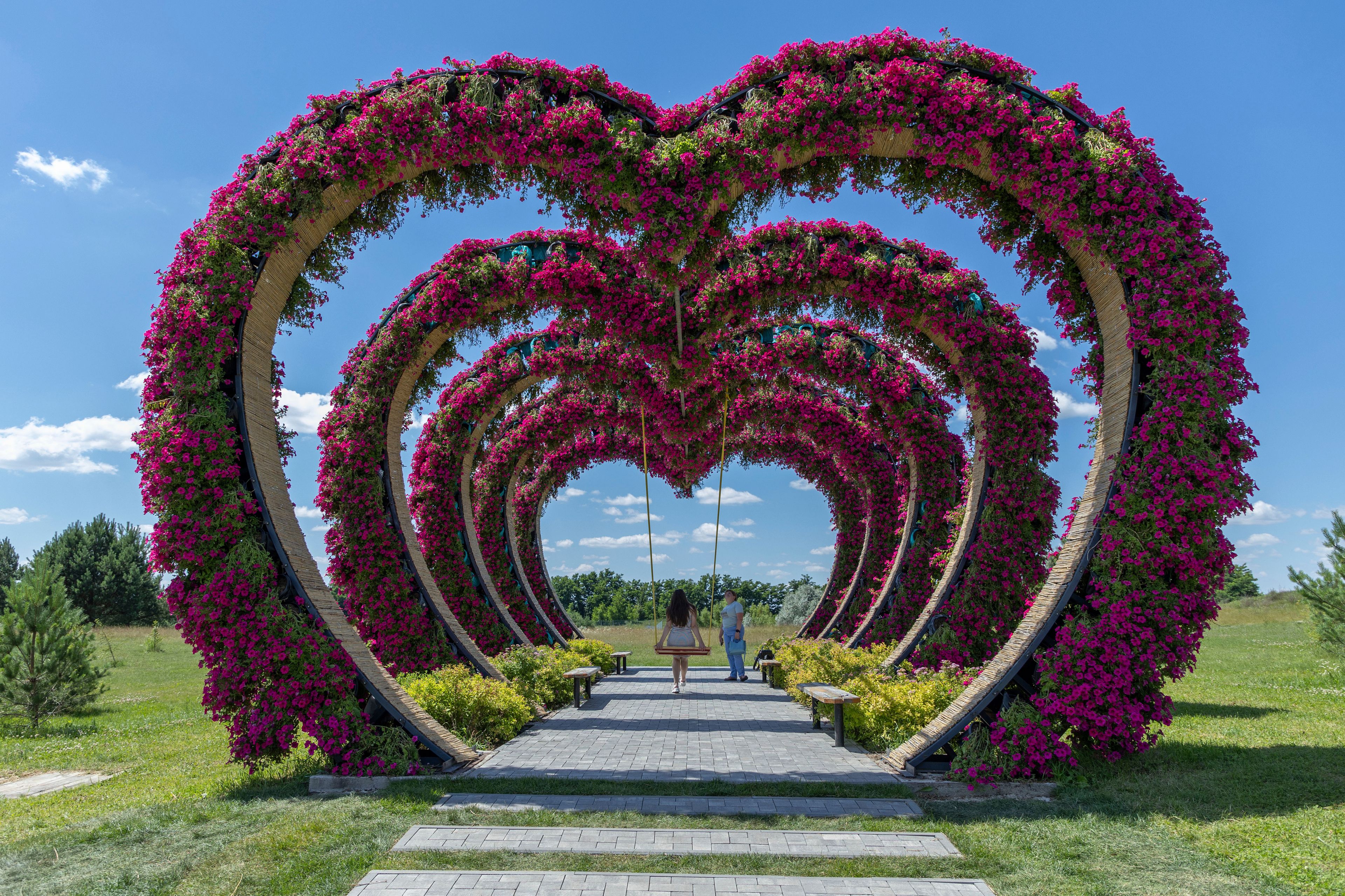 A woman swings from a heart-shaped flower installation in Dobro Park, Motyzhyn, Kyiv region, Ukraine, Wednesday, June 26, 2024. Despite hardships brought by war flowers fill Kyiv and other Ukrainian cities. They burst out of planters that line the capital's backroads and grand boulevards and are fixed to lampposts. (AP Photo/Anton Shtuka)