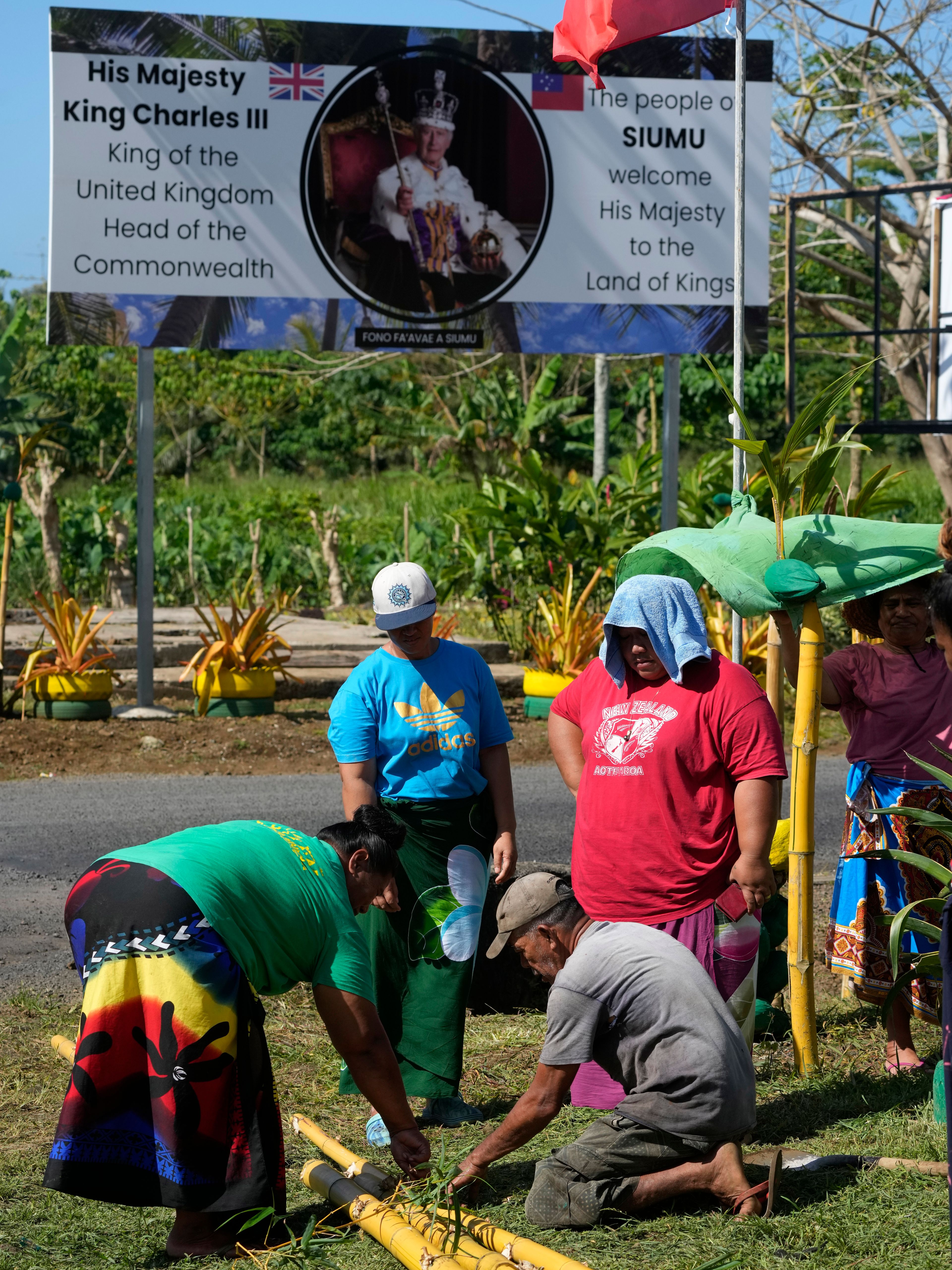 People from the village of Siumu, Samoa, work on decorating the entrance of their village on Monday, Oct. 21, 2024, as they prepare for the arrival of King Charles III. (AP Photo/Rick Rycroft)