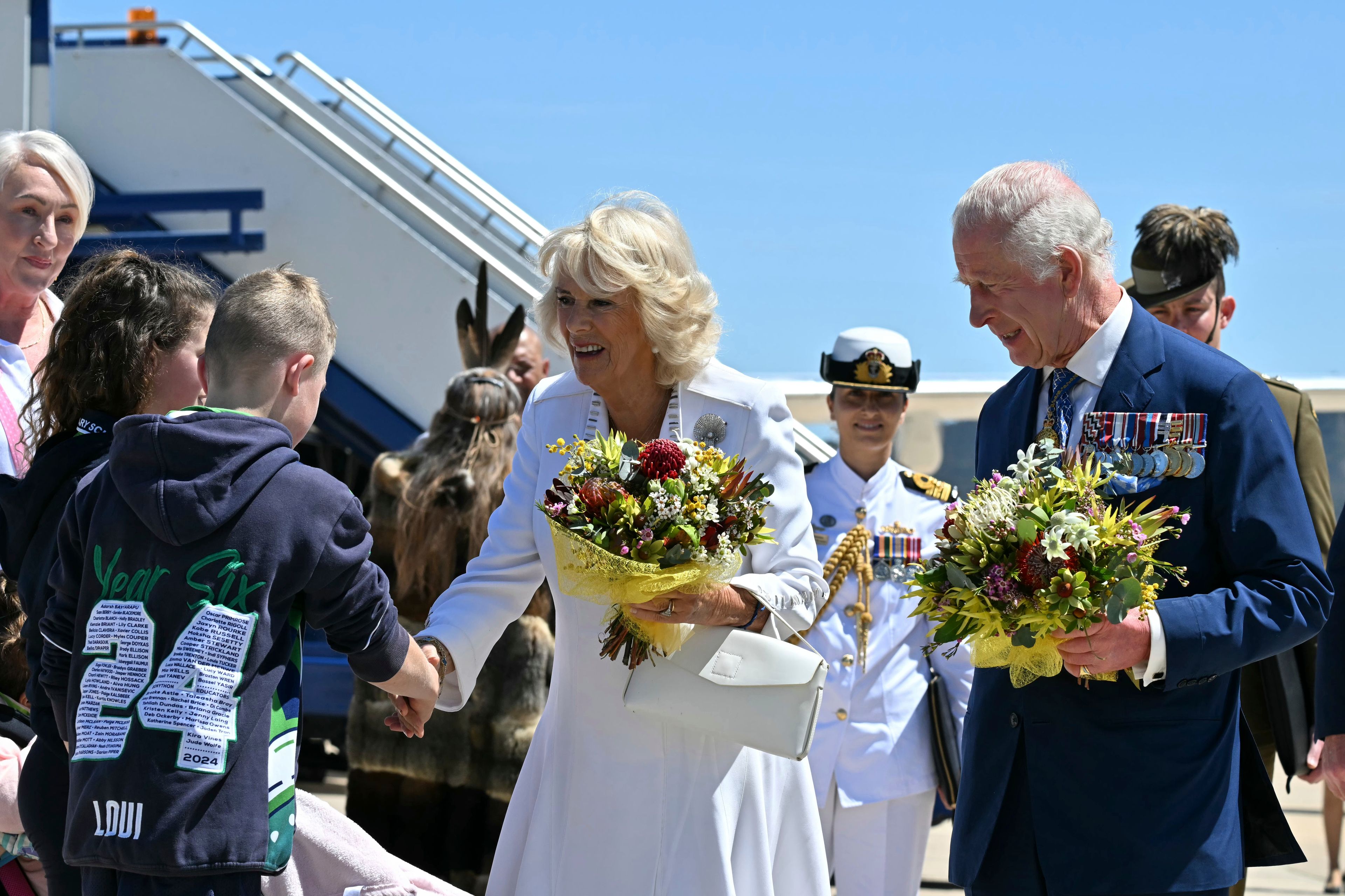 Britain's King Charles III, right, and Queen Camilla, center, receive flowers after arriving at Defense Establishment Fairbairn in Canberra, Australia, Monday, Oct. 21, 2024. (Saeed Khan/Pool Photo via AP)