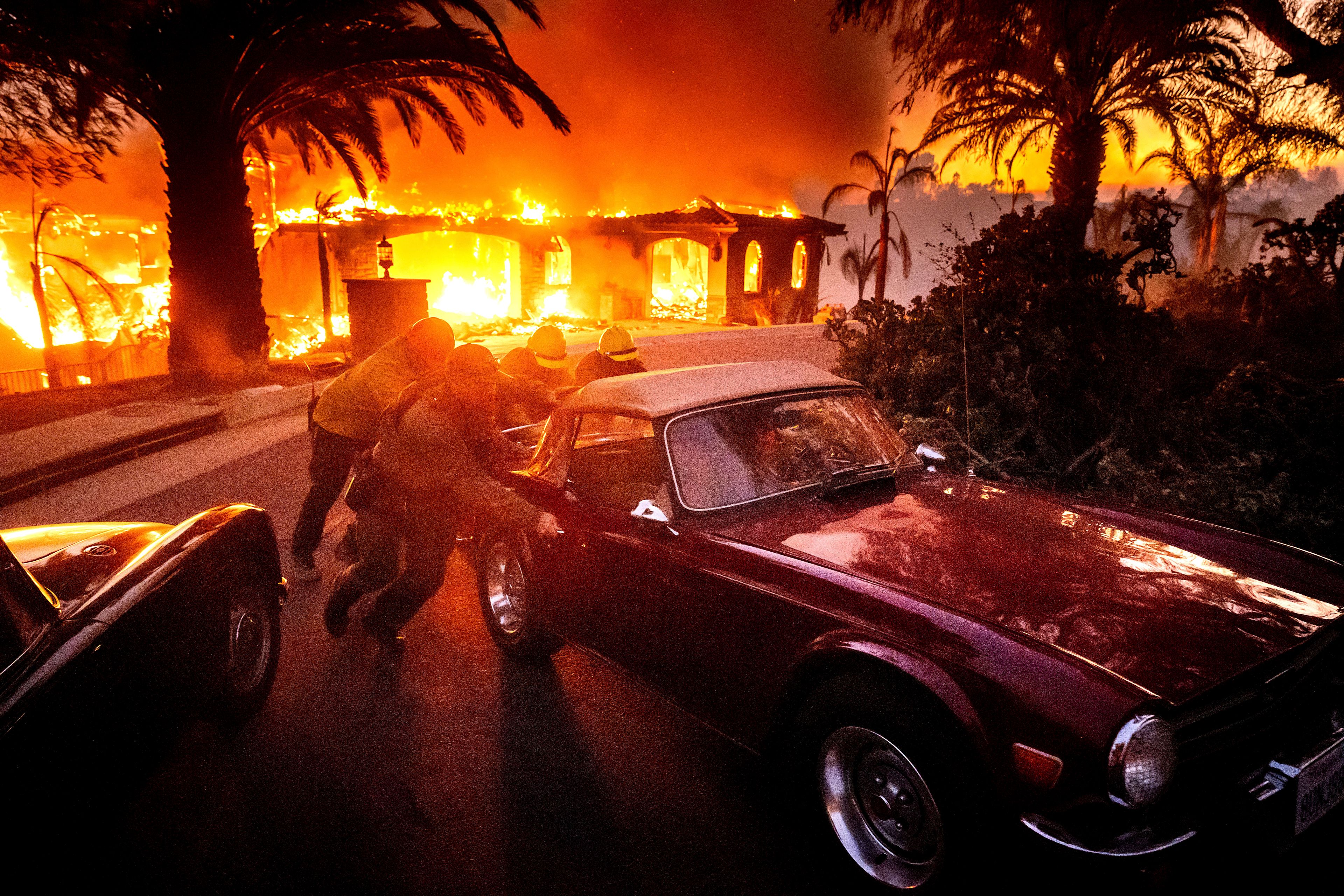 CORRECTS CAR - Firefighters and sheriff's deputies push a vintage car away from a burning home as the Mountain Fire burns in Camarillo, Calif., on Wednesday, Nov. 6, 2024. (AP Photo/Noah Berger)