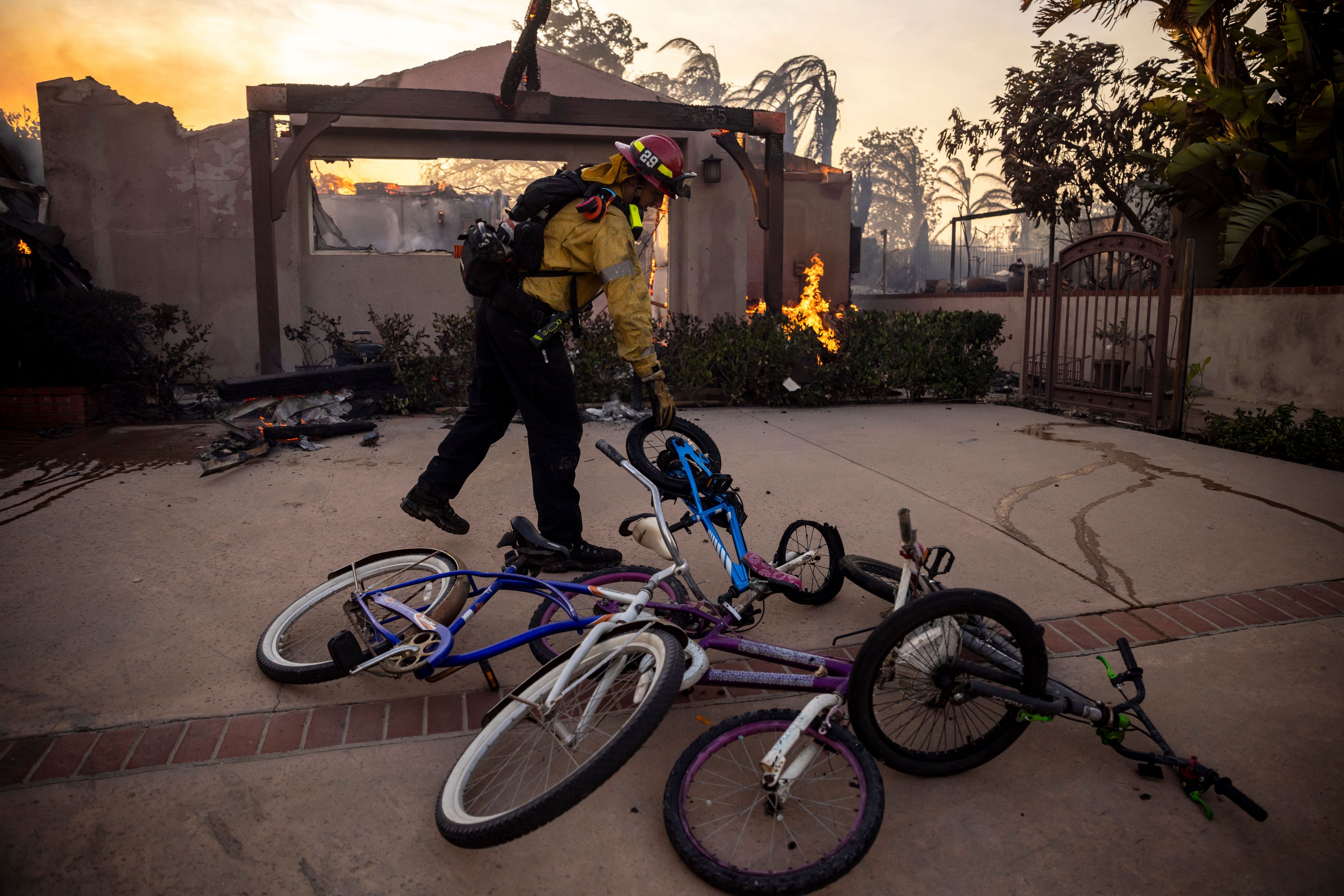 A firefighter, moves bicycles as he works against the Mountain fire, Wednesday, Nov. 6, 2024, near Camarillo, Calif. (AP Photo/Ethan Swope)